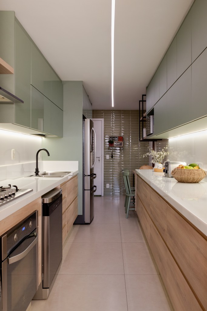 ape-150-m-cozinha-tom-verde-suave-estante-vazada-ana-cano-03 Apê de 150 m² ganha cozinha em tom verde suave e estante vazada na sala. Projeto de Ana Cano. Na foto, cozinha estreita, bancada branca.