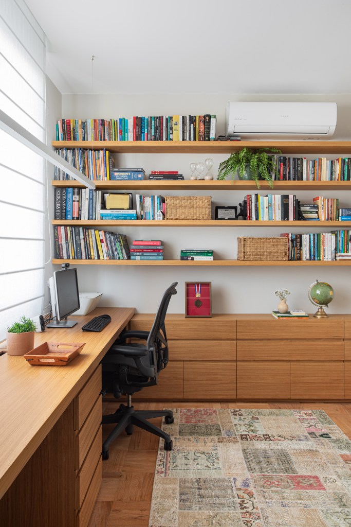 Reforma restaura piso de peroba e cria duas suítes em apê de 360 m². Projeto de Escala Arquitetura. Na foto, home office, prateleira com livros, bancada de madeira.