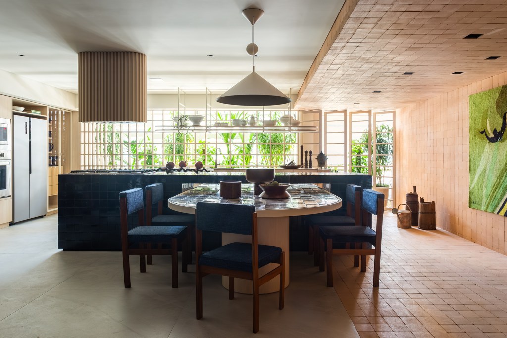 Cerâmicas artesanais compõem o tampo da mesa desta cozinha repleta de azul. Projeto de Mandril Arquitetura. Na foto, cozinha com bancada azul, mesa de azulejos e tijolinhos.