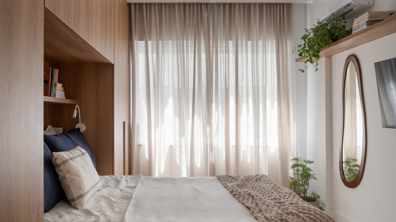 Espelho oval e armário em volta da cama são destaques em apê de 67 m². Projeto de Mariana Monnerat. Na foto, quarto, cortina, plantas, cama de casal.