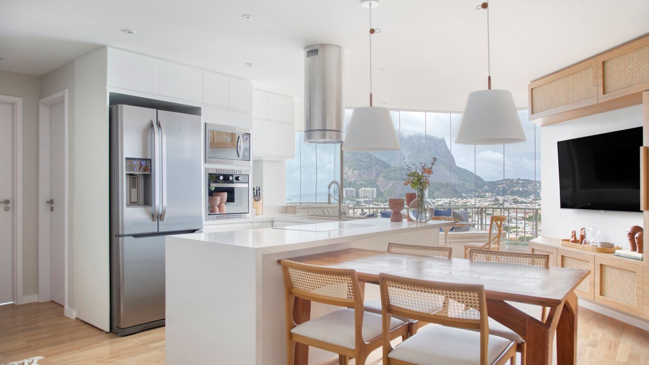 Laca na decoração: veja vantagens, mitos e como cuidar de peças laqueadas. Projeto de Memoá Arquitetos. Na foto, cozinha integrada com ilha branca, mesa de madeira.
