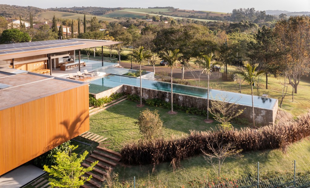 Piscina com muro de pedra dois volumes distintos compõem casa de 700 m². Projeto de Padovani Arquitetos. Na foto, fachada com jardim. Piscina com muro de pedra.