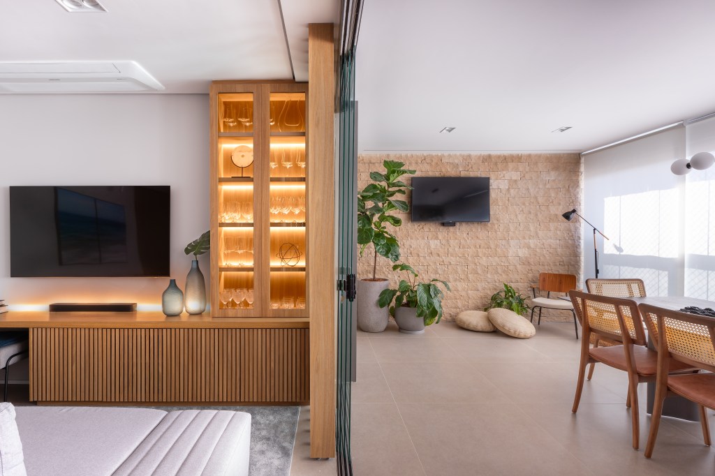 Apartamento de 110 m² destaca parede de brick e materiais naturais. Projeto do Martins Galera Arquitetura. Na foto, varanda gourmet e sala de estar divididas por porta de vidro