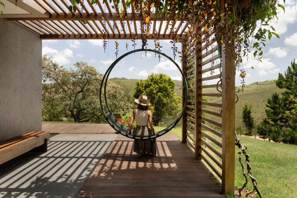 Sintonia com natureza: casa de campo com lareira tem sofá e cozinhas roxos. Projeto de Camila Medrado. Na foto, jardim, pergolado, cadeira de balanço.