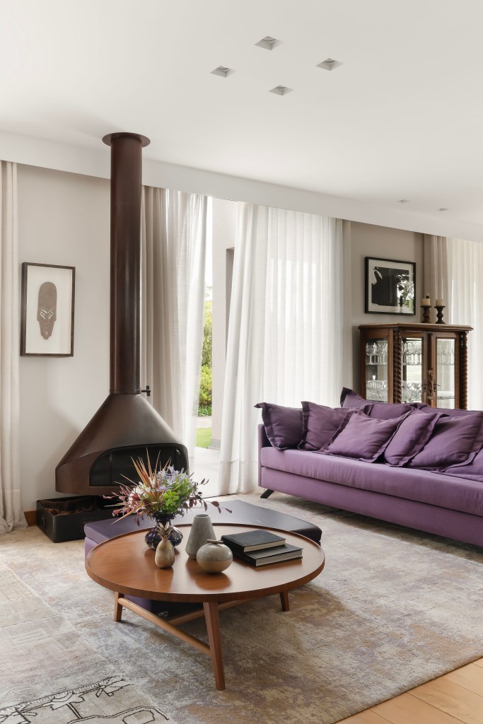 casa-de-campo-lareira-sofa-cozinhas-roxos-camila-medrado-10-sala Sintonia com natureza: casa de campo com lareira tem sofá e cozinhas roxos. Projeto de Camila Medrado. Na foto, sala de estar, lareira, cortina.