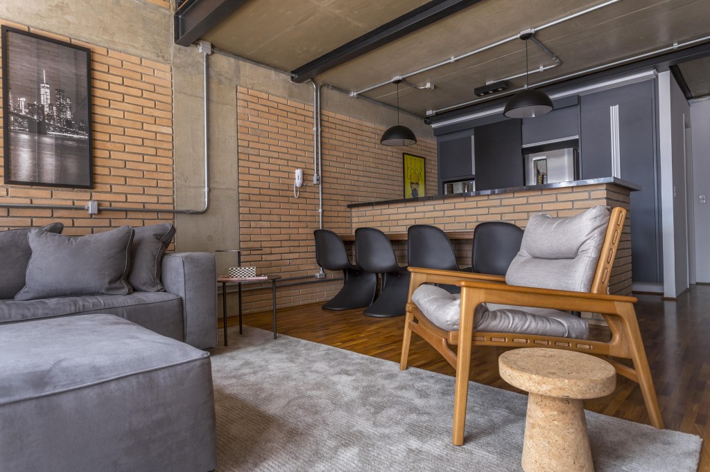 Cores naturais: veja quais são os tons mais populares com projetos e dicas. Projeto de Korman Arquitetos. Na foto, sala industrial, parede de tijolinhos, sofá cinza.