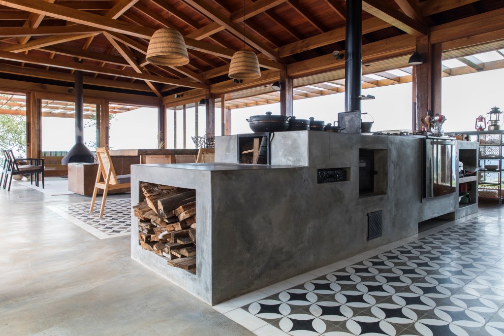 Linda casa na montanha tem lareira e cozinha rústica com fogão à lenha. Projeto de Sabella Arquitetura. Na foto, cozinha integrada, tapete de ladrilhos.