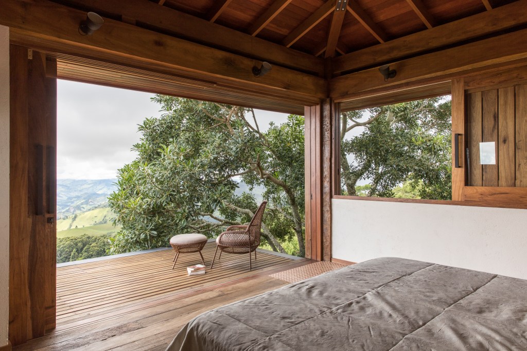 Linda casa na montanha tem lareira e cozinha rústica com fogão à lenha. Projeto de Sabella Arquitetura. Na foto, quarto rústico, piso e parede de madeira.