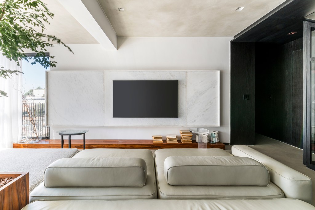 Apê preto e branco tem cobertura retrátil em vidro que abriga jacuzzi. Projeto de Liró Arquitetura. Na foto, sala, sofá, painel de tv.