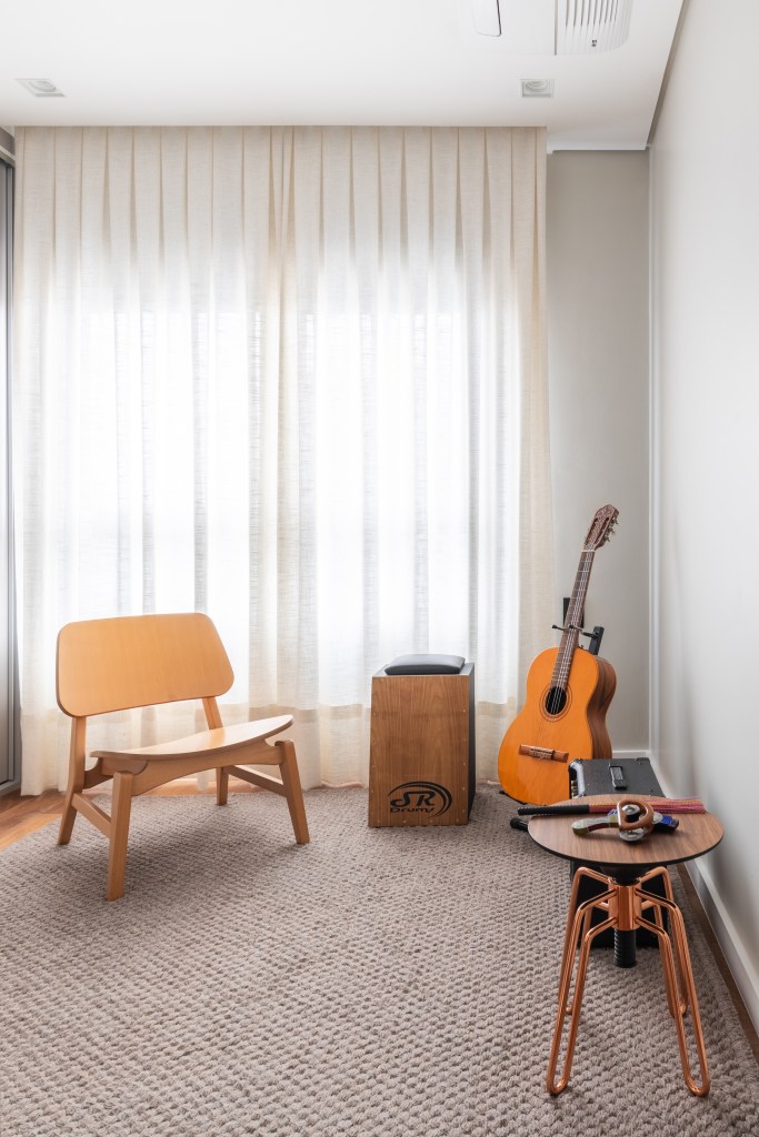 Bancada de lâmina sintetizada integra cozinha e área gourmet neste apartamento. Projeto de BMA Studio. Na foto, quarto, cadeira de madeira, cortina, violão.