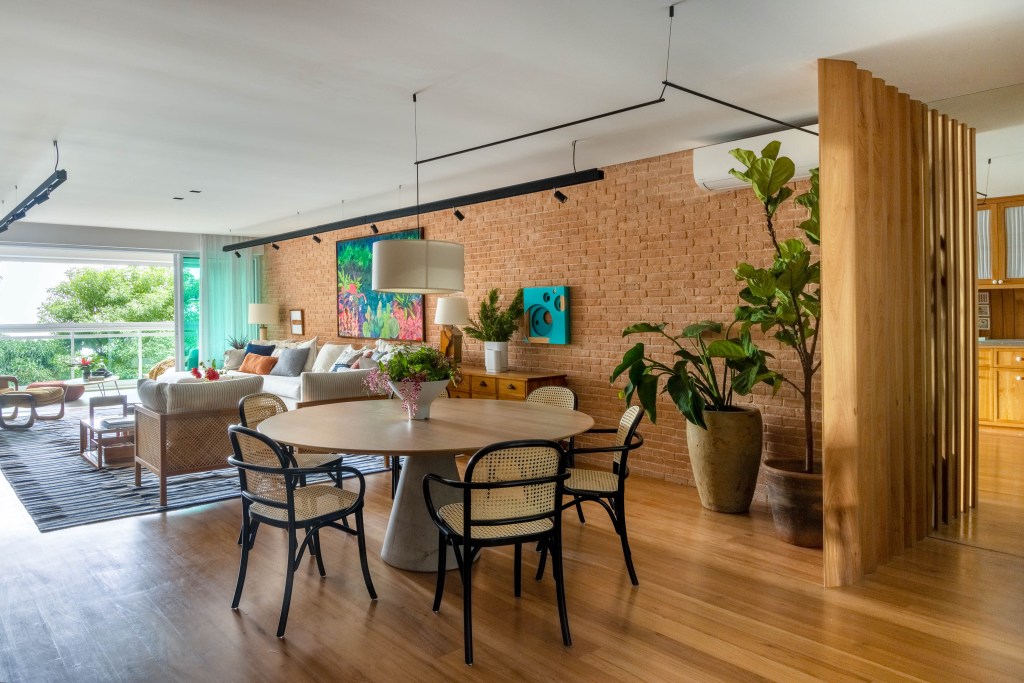 Cozinha de apê tem armário verde oliva, azulejo branco e paredes com toque preto. Projeto de Escala Arquitetura. Na foto, sala de estar, mesa redonda, parede de tijolinhos.