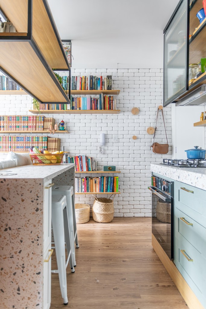 Miniapê de 25 m² tem sofá de canto alemão com baú e estante de mil livros. Projeto de Lemarchi Arquitetura. Na foto, cozinha, parede de tijolinhos brancos, bancada com revestimento colorido estilo granilite.