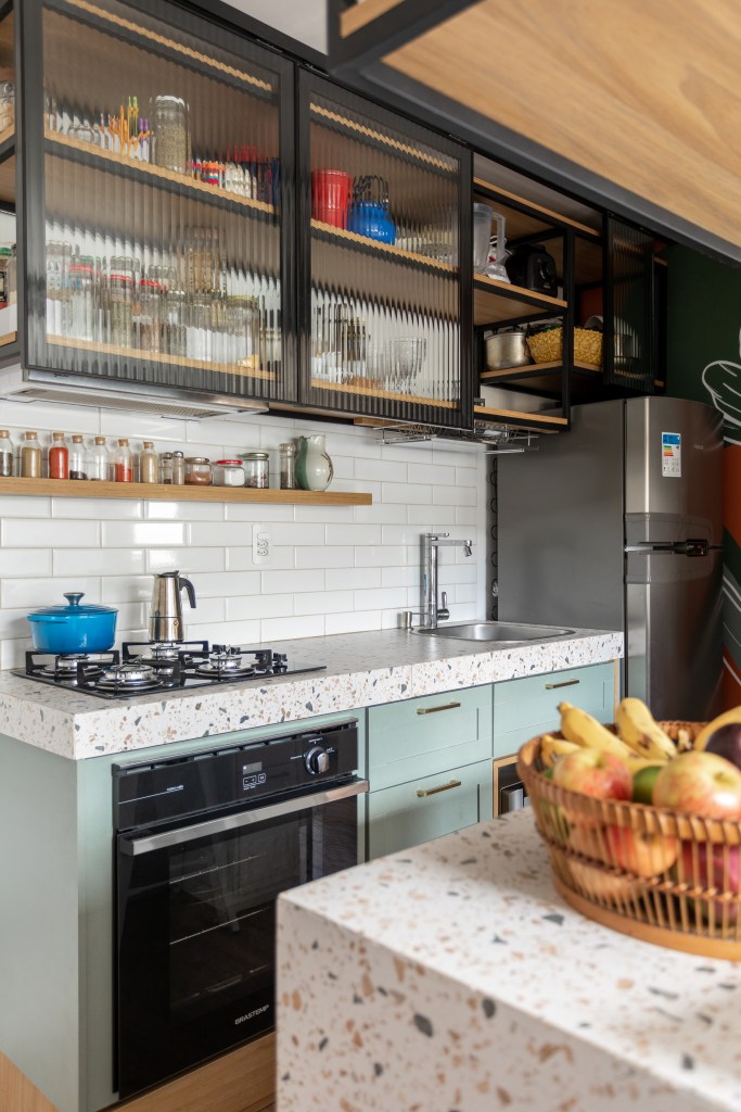 Miniapê de 25 m² tem sofá de canto alemão com baú e estante de mil livros. Projeto de Lemarchi Arquitetura. Na foto, cozinha, prateleiras com temperos, bancada com revestimento estilo granilite.