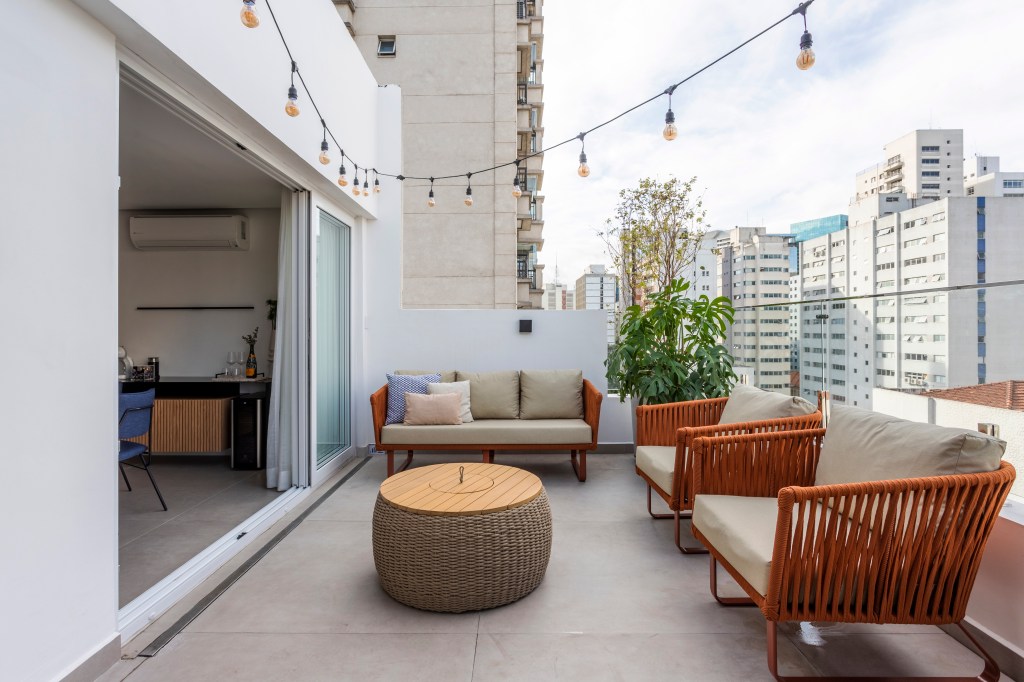 Terraço com churrasqueira, cervejeira e chopeira é local perfeito para lazer em apê. Projeto do Estúdio Bena. Na foto, varanda, sofá e poltronas para área externa, luzes.