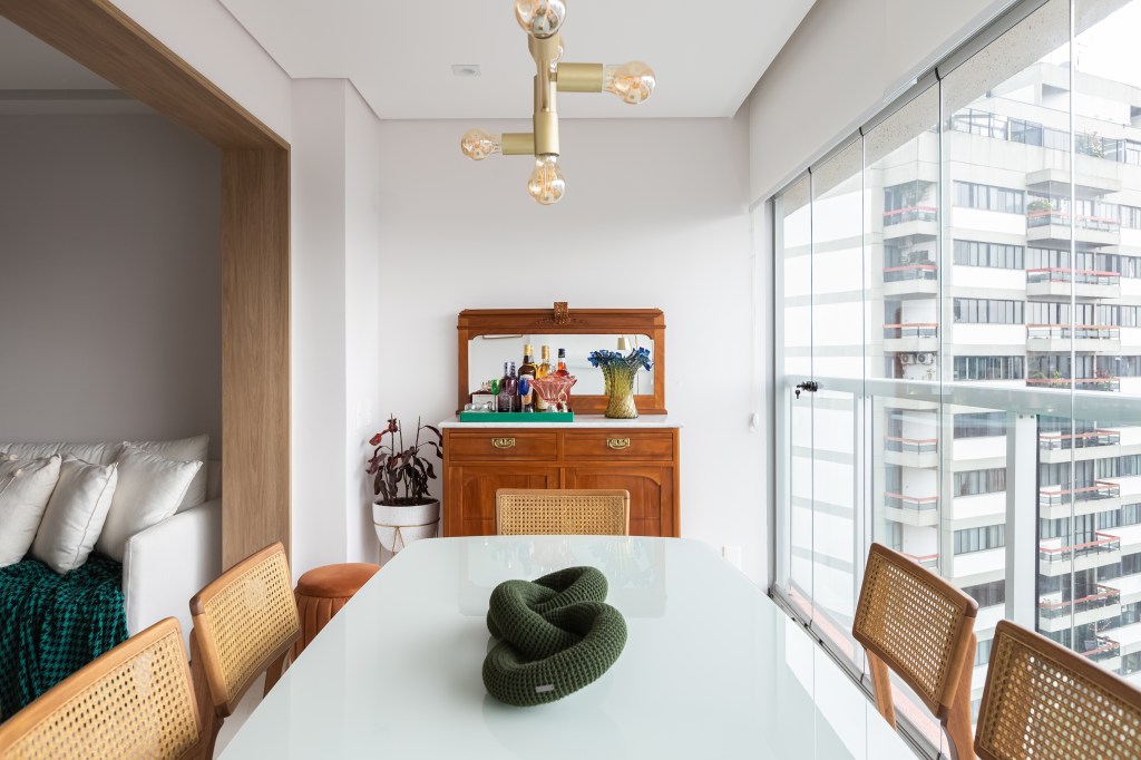 Móvel antigo funciona como bar e apoio para a mesa de jantar em apê de 69 m²